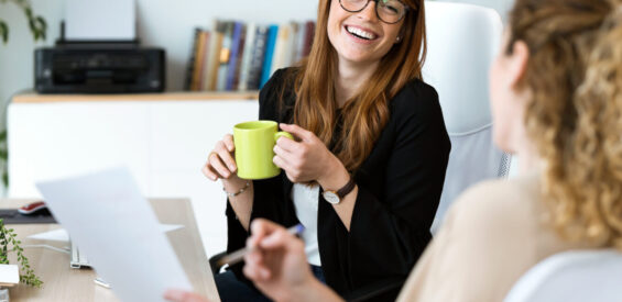 Two pretty young business woman relaxing one moment while drinking coffee in the office.